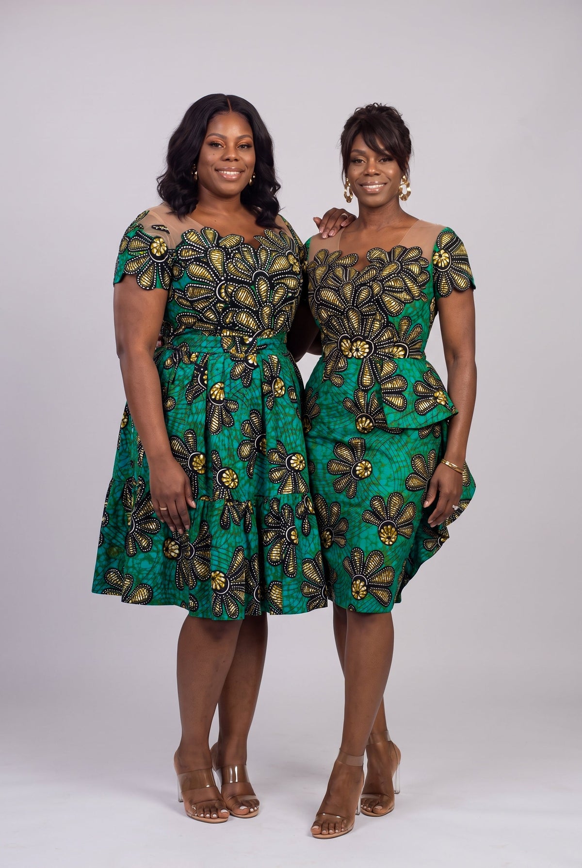 Two women wearing green and gold African print wedding guest dresses