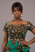 A woman modeling a vibrant green African print dress with large gold and black floral applique details.