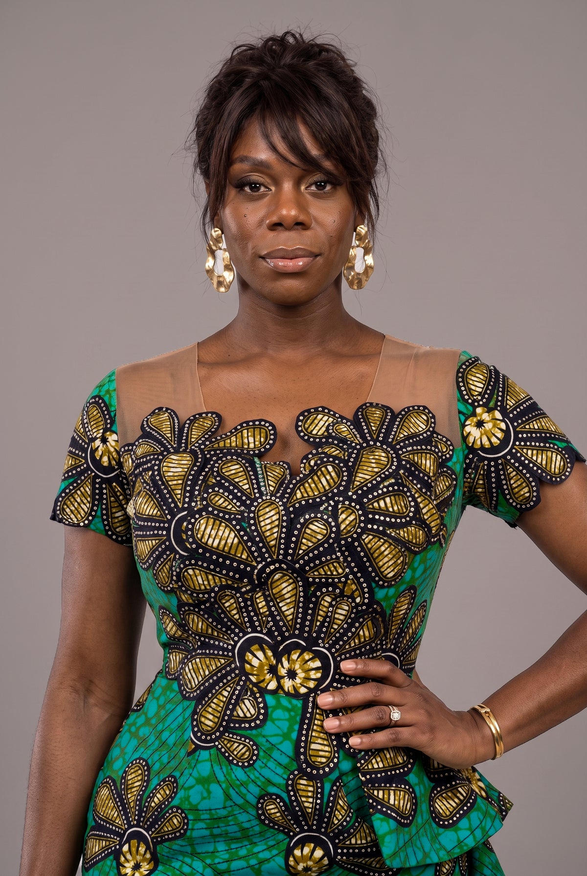 A woman modeling a vibrant green African print dress with large gold and black floral applique details.