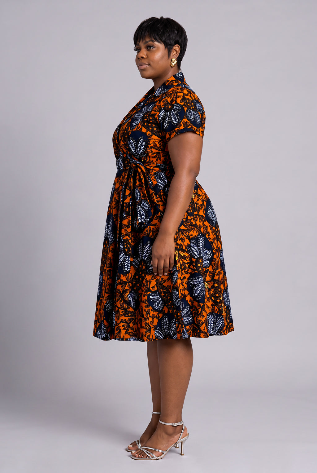 A woman modeling a short-sleeve Ankara wrap dress with  a bold orange, black, and blue floral print 