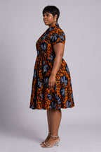 A woman modeling a short-sleeve Ankara wrap dress with  a bold orange, black, and blue floral print 