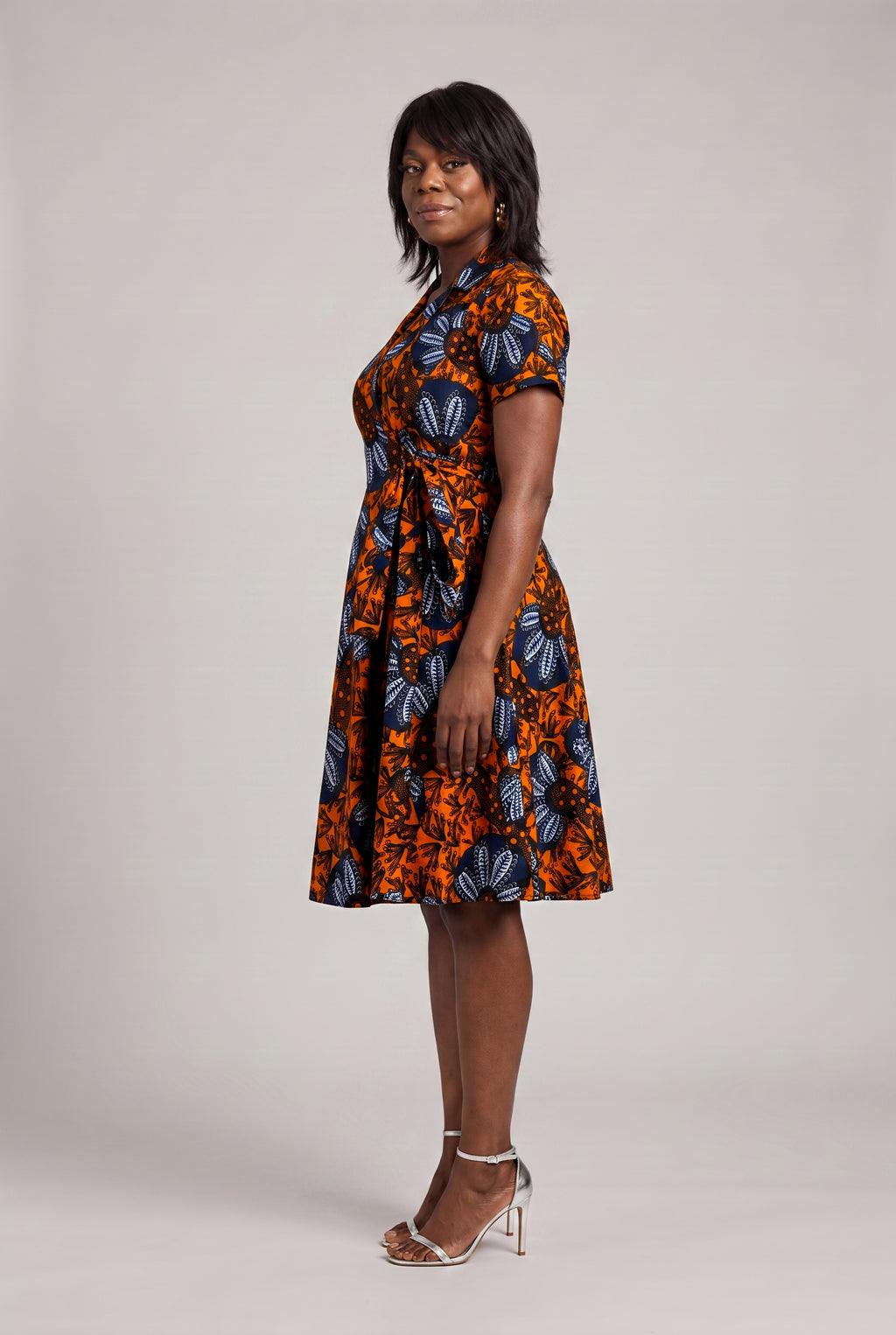 Side view of orange and navy African print wrap dress with fitted waist 
