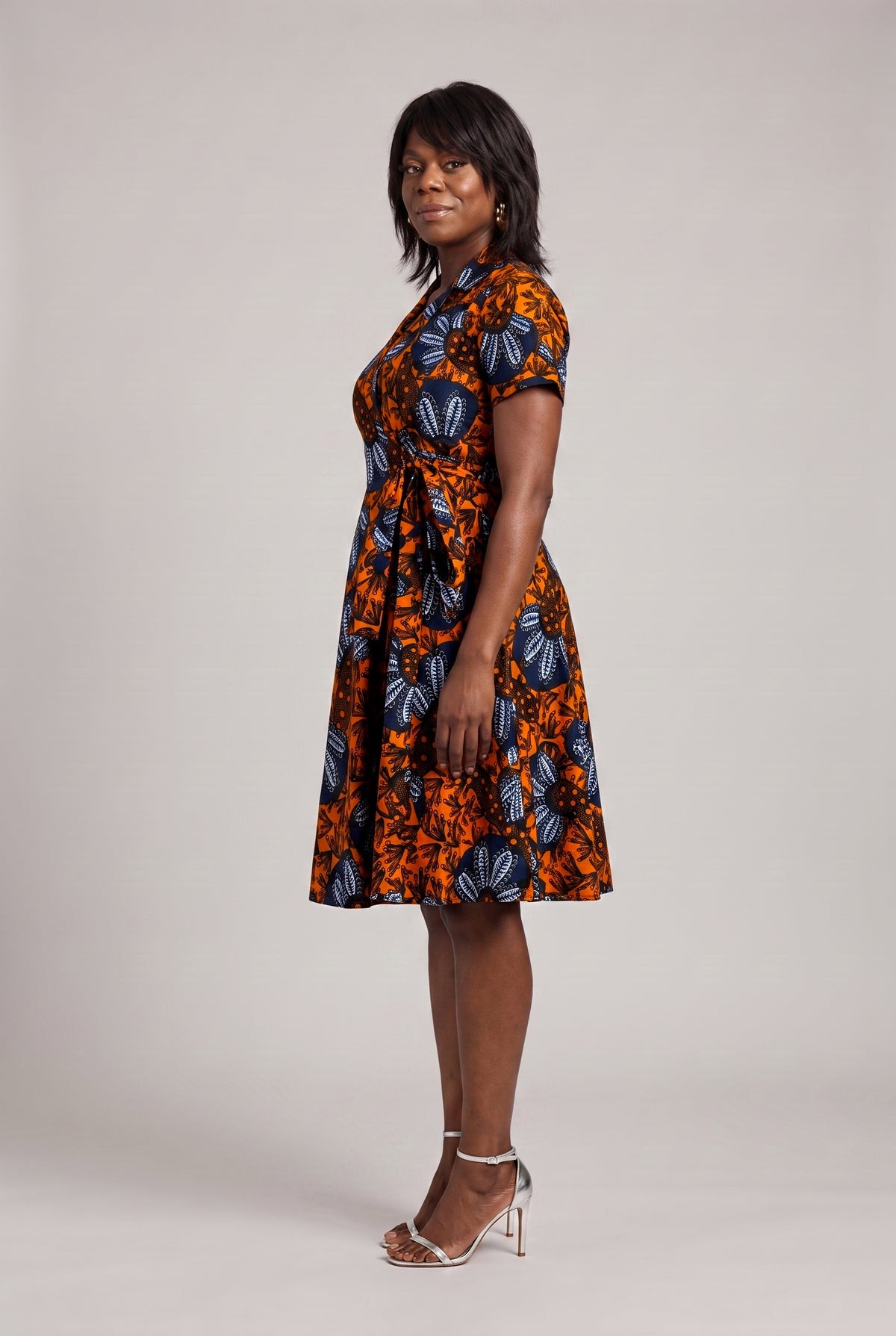 Side view of orange and navy African print wrap dress with fitted waist 