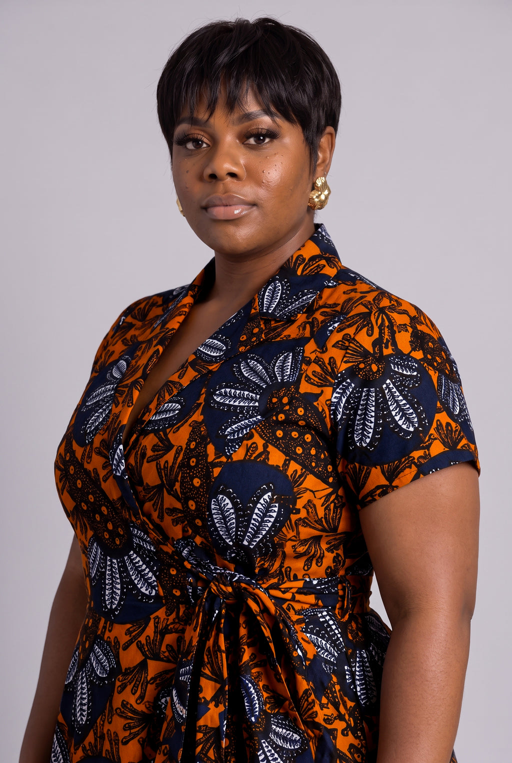 Side profile view of model wearing a short-sleeve African wrap dress with a bold orange, navy, and white floral pattern