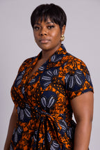 Side profile view of model wearing a short-sleeve African wrap dress with a bold orange, navy, and white floral pattern