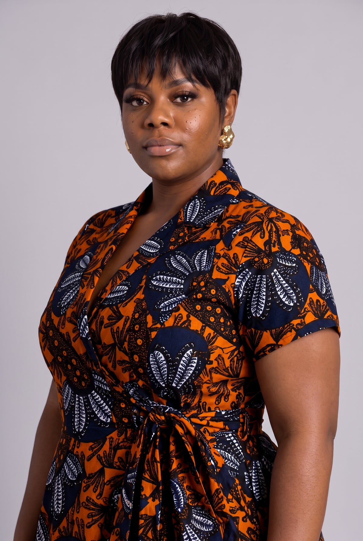 Side profile view of model wearing a short-sleeve African wrap dress with a bold orange, navy, and white floral pattern