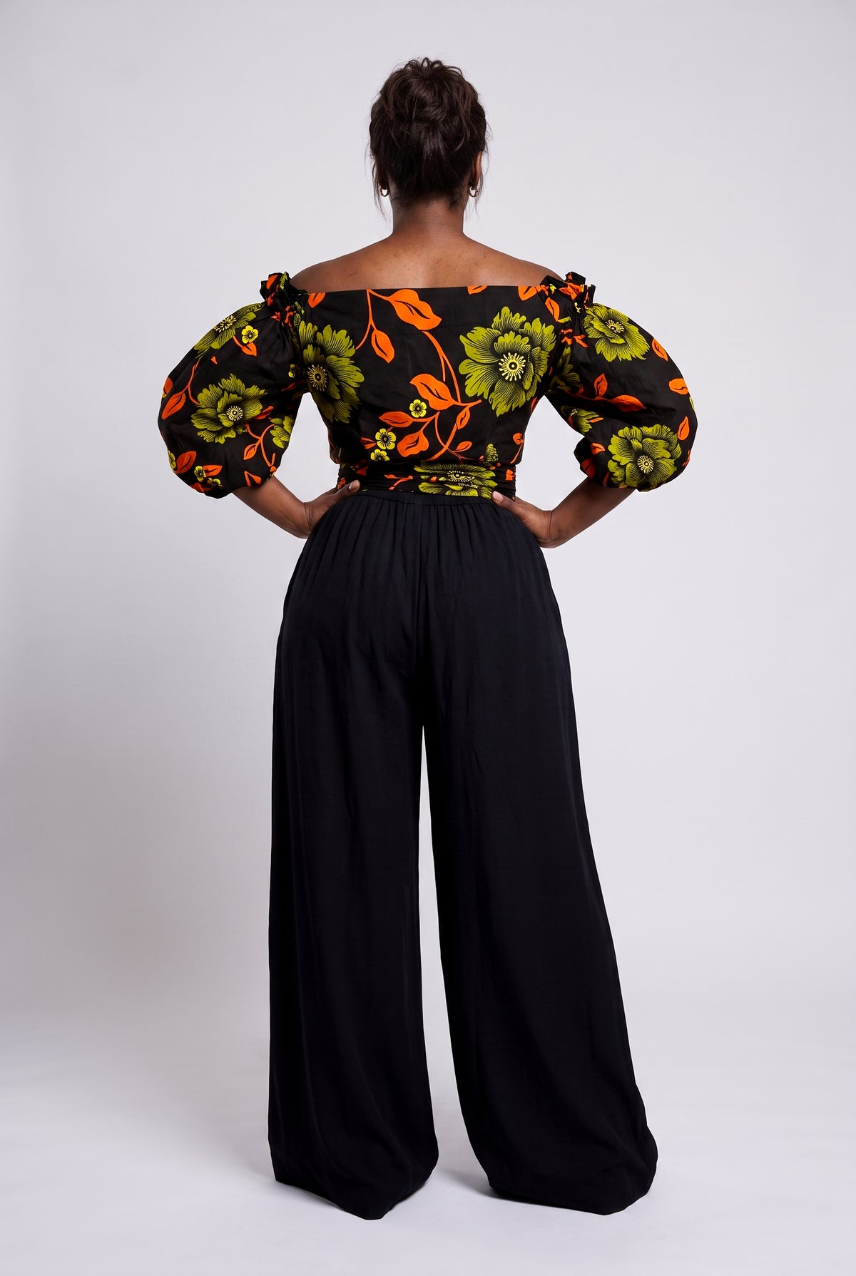 Back view of Olive Oasis orange and green African print wrap top worn with black palazzo trousers
