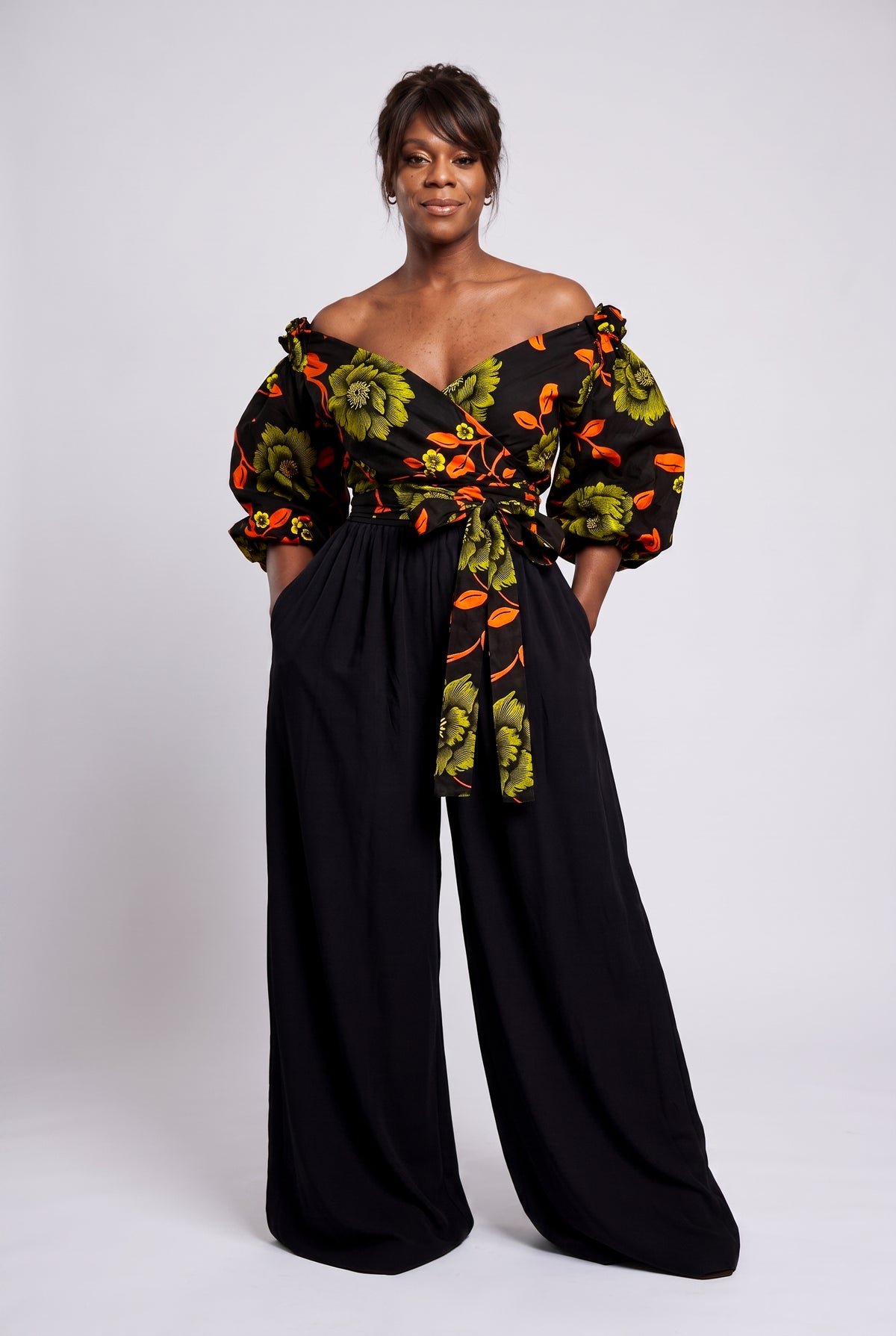 Model wearing Olive Oasis orange and green African print Ankara off shoulder wrap top with short puff sleeves