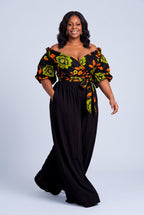 Woman walking in Olive Oasis African print wrap top with black palazzo trousers
