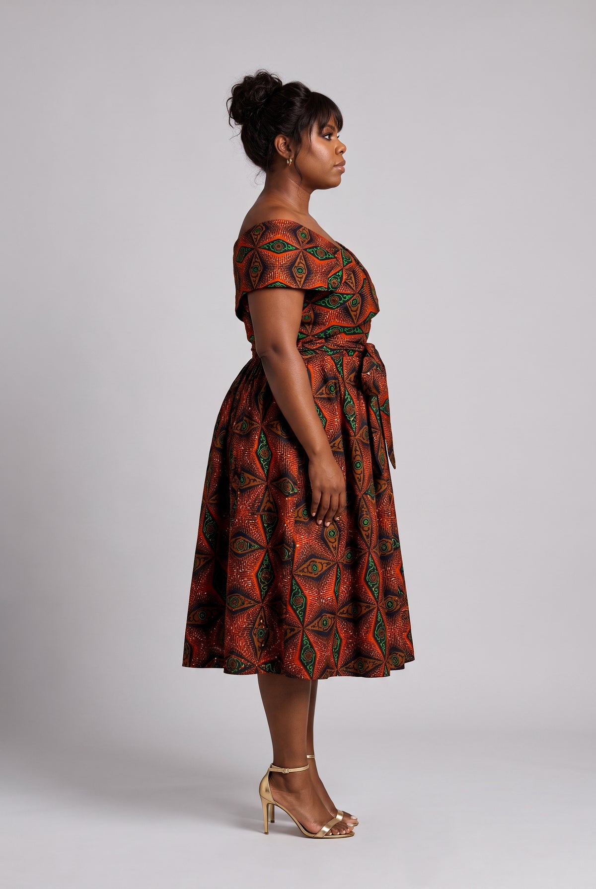 Side profile view of a curvy model wearing orange African print dress